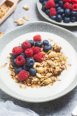 Granola with yogurt, raspberries, blueberries in a plate on a gray background