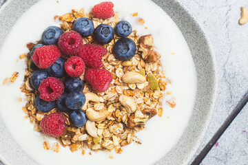 Granola with yogurt, raspberries, blueberries in a plate on a gray background