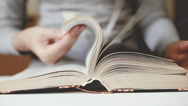 Women's hands hold a book and leaf through the pages. Student preparing for the exam and reading literature