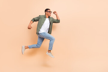 Fototapeta na wymiar Full length photo of pretty excited man wear khaki shirt running hurrying jumping high empty space isolated beige color background