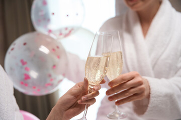 Cheerful young females in bathrobes drinking champagne