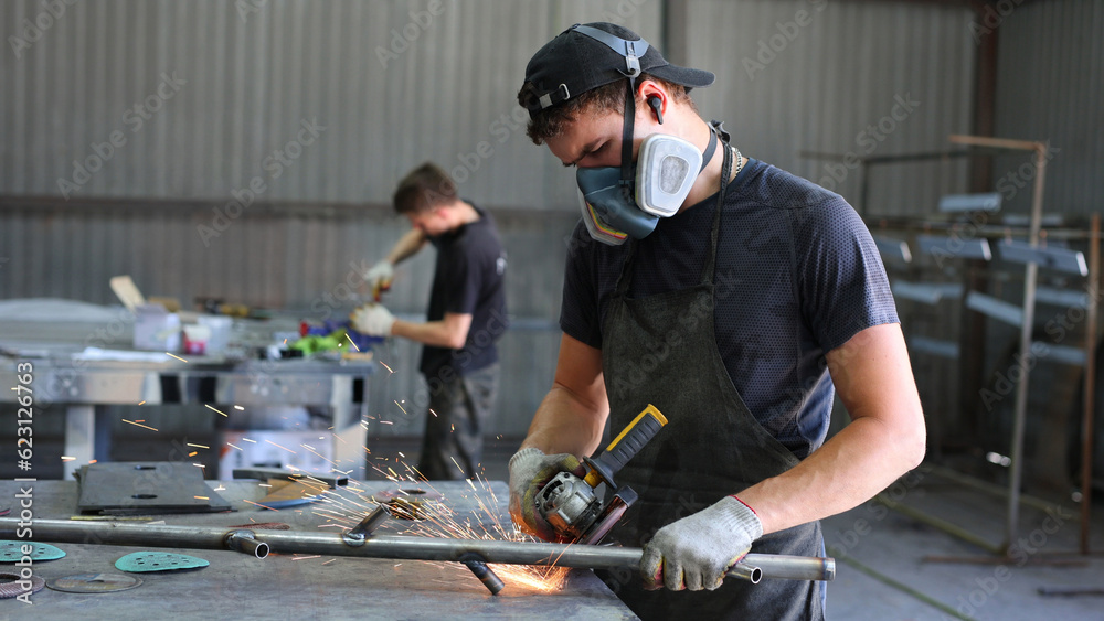 Wall mural Metalworking workshop. The master grinds the metal with a grinding machine. Sparks