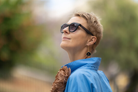 Adult stylish woman with short hair with a big accessory on her jacket wearing sunglasses and pretty big earrings - looking up