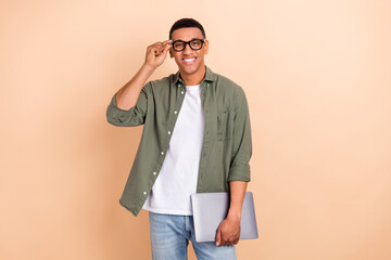 Photo of satisfied smart cheerful positive guy dressed khaki shirt touching glasses holding laptop...