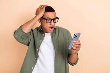 Photo of worried stressed confused guy dressed khaki shirt glasses look at smartphone hand on head isolated on pastel color background
