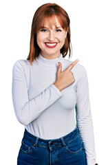 Fototapeta premium Redhead young woman wearing casual turtleneck sweater cheerful with a smile on face pointing with hand and finger up to the side with happy and natural expression