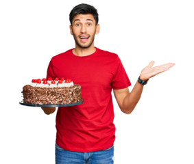 Young handsome man celebrating birthday with cake celebrating victory with happy smile and winner expression with raised hands