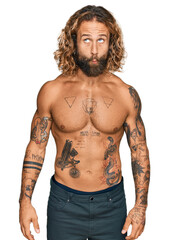Fototapeta premium Handsome man with beard and long hair standing shirtless showing tattoos making fish face with lips, crazy and comical gesture. funny expression.