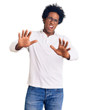 Handsome african american man with afro hair wearing casual clothes and glasses afraid and terrified with fear expression stop gesture with hands, shouting in shock. panic concept.