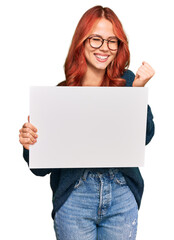Naklejka premium Young redhead woman holding blank empty banner screaming proud, celebrating victory and success very excited with raised arms