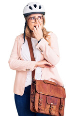 Young caucasian woman wearing bike helmet and leather bag looking stressed and nervous with hands on mouth biting nails. anxiety problem.
