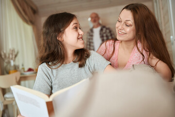 Joyous teenage girl doing homework with help of mom