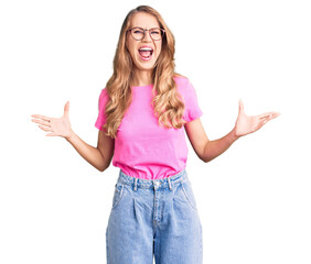 Fototapeta na wymiar Young beautiful caucasian woman with blond hair wearing casual clothes and glasses crazy and mad shouting and yelling with aggressive expression and arms raised. frustration concept.