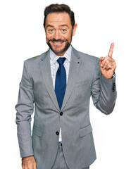 Middle age man wearing business clothes with a big smile on face, pointing with hand finger to the side looking at the camera.