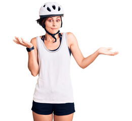 Beautiful young woman with short hair wearing bike helmet clueless and confused expression with arms and hands raised. doubt concept.