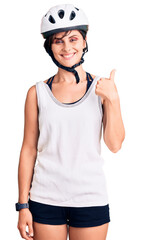 Beautiful young woman with short hair wearing bike helmet smiling happy and positive, thumb up doing excellent and approval sign