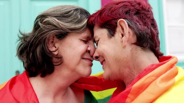 Senior gay lesbian couple having tender moment wearing Lgbtq rainbow flag at pride parade - Family and love concept - Powered by Adobe