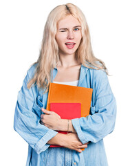 Young caucasian woman holding books winking looking at the camera with sexy expression, cheerful and happy face.