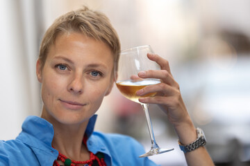 An adult stylish woman holding a glass on wine outdoors - looking in the camera