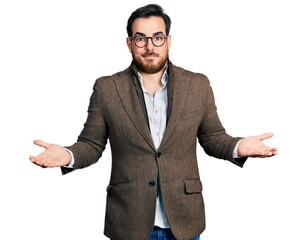 Young hispanic man wearing business jacket and glasses clueless and confused expression with arms and hands raised. doubt concept.