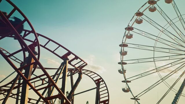 Entertainment for children during school holidays. Twisting red roller coaster and Ferris wheel Silhouettes at sunset. Funfair and amusement park