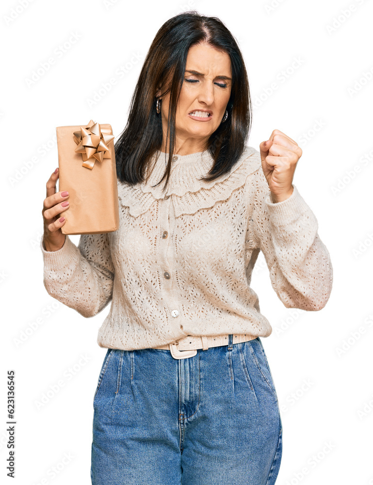 Sticker Middle age brunette woman holding gift annoyed and frustrated shouting with anger, yelling crazy with anger and hand raised