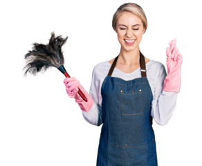 Beautiful young blonde woman wearing apron holding cleaning duster gesturing finger crossed smiling with hope and eyes closed. luck and superstitious concept.