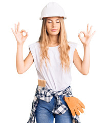 Beautiful caucasian woman with blonde hair wearing hardhat and painter clothes relax and smiling with eyes closed doing meditation gesture with fingers. yoga concept.