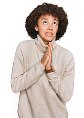 Young hispanic girl wearing wool winter sweater begging and praying with hands together with hope expression on face very emotional and worried. begging.