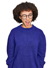 Young hispanic girl wearing casual winter sweater and glasses winking looking at the camera with...