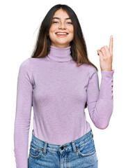 Young beautiful teen girl wearing turtleneck sweater showing and pointing up with finger number one while smiling confident and happy.