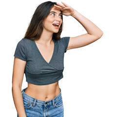 Young beautiful teen girl wearing casual crop top t shirt very happy and smiling looking far away with hand over head. searching concept.