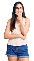 Young beautiful caucasian woman wearing casual clothes and glasses looking confident at the camera smiling with crossed arms and hand raised on chin. thinking positive.