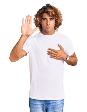 Young hispanic man wearing casual white tshirt swearing with hand on chest and open palm, making a loyalty promise oath