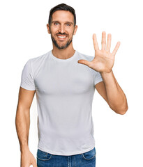 Fototapeta premium Handsome man with beard wearing casual white t shirt showing and pointing up with fingers number five while smiling confident and happy.