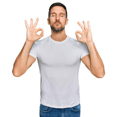 Fototapeta premium Handsome man with beard wearing casual white t shirt relax and smiling with eyes closed doing meditation gesture with fingers. yoga concept.