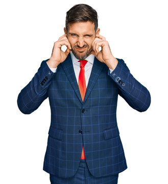 Handsome man with beard wearing business suit and tie covering ears with fingers with annoyed expression for the noise of loud music. deaf concept.