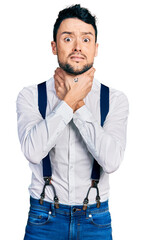 Hispanic man with beard wearing hipster look with bow tie and suspenders shouting and suffocate because painful strangle. health problem. asphyxiate and suicide concept.