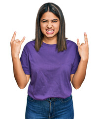 Young hispanic girl wearing casual purple t shirt shouting with crazy expression doing rock symbol with hands up. music star. heavy concept.