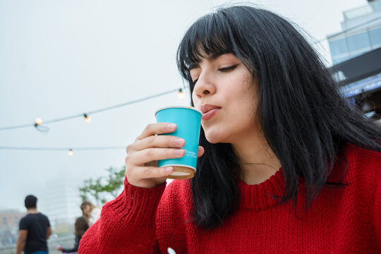 young Latin woman blowing on the coffee because it is too hot to drink
