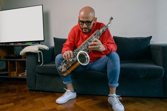 young latino musician man studying at home holds his saxophone and is thinking how to make the chord