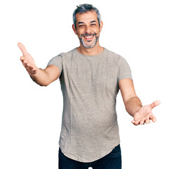 Middle age hispanic with grey hair wearing casual grey t shirt looking at the camera smiling with open arms for hug. cheerful expression embracing happiness.