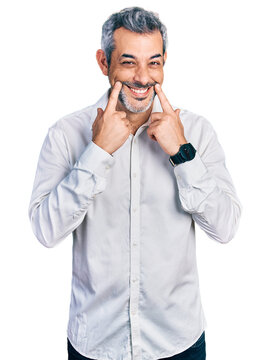 Middle age hispanic with grey hair wearing casual white shirt smiling with open mouth, fingers pointing and forcing cheerful smile