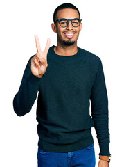 Naklejka premium Young african american man wearing casual clothes and glasses showing and pointing up with fingers number two while smiling confident and happy.