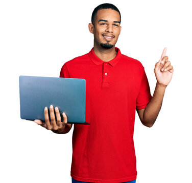Young african american man working using computer laptop surprised with an idea or question pointing finger with happy face, number one