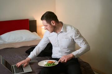 Focused guy using portable computer during lunch in aparthotel
