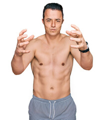 Fototapeta premium Handsome young man wearing swimwear shirtless shouting frustrated with rage, hands trying to strangle, yelling mad