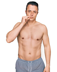 Fototapeta premium Handsome young man wearing swimwear shirtless mouth and lips shut as zip with fingers. secret and silent, taboo talking
