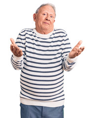 Senior handsome grey-haired man wearing casual striped sweater clueless and confused expression with arms and hands raised. doubt concept.