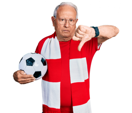 Senior man with grey hair football hooligan holding ball looking unhappy and angry showing rejection and negative with thumbs down gesture. bad expression.